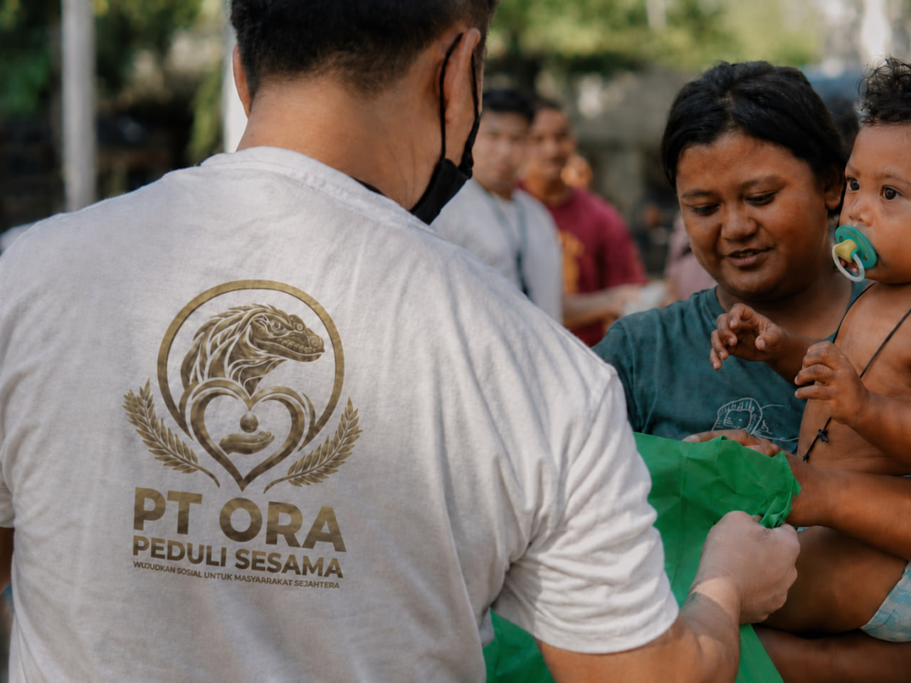 Penyerahan paket kebutuhan kepada pengasuh yang menggendong anak